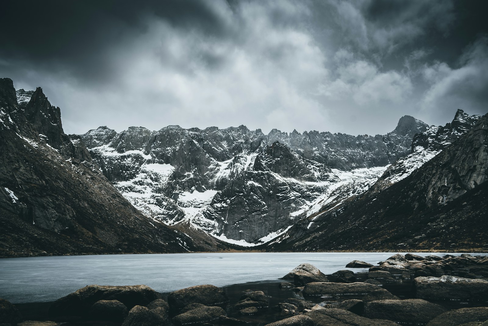 Snow-covered alpine peaks rising above a still lake under dramatic clouds